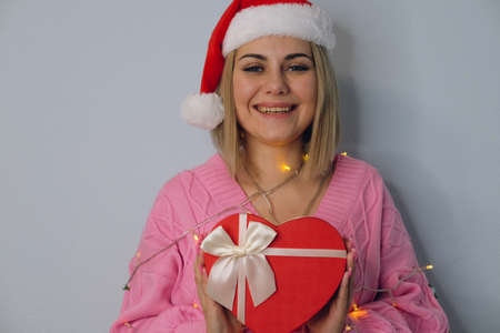 Beautiful girl in a hat of Santa Claus, decorated with New Year's lanterns with a gift in her hands, close-up. The concept of Christmas and New Yearの写真素材