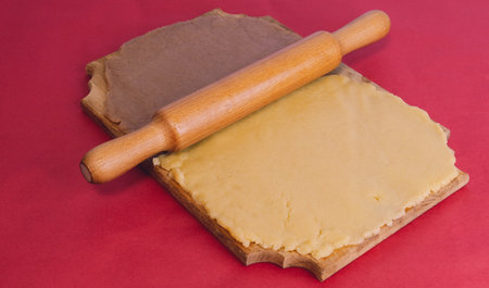 Dough for making homemade gingerbread cookies on a wooden board on a red background.の写真素材