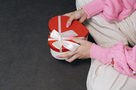 Girl holding a gift in a red box in the shape of a heart. Dark background, selective focus. Concept black friday, holiday, birthday, womens dayの写真素材
