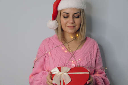 Beautiful girl in a hat of Santa Claus, decorated with New Year's lanterns with a gift in her hands, close-up. The concept of Christmas and New Yearの写真素材