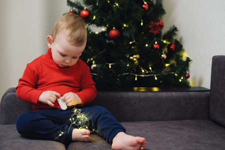 Portrait of a little child on the background of a Christmas tree. Boy plays with a gift. Concept - Christmas and New Yearの写真素材