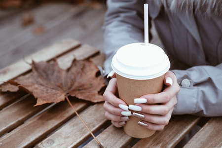 Female hand on the background of a wooden table with a paper cup of takeaway coffeeの写真素材