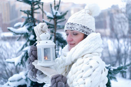Portrait of a beautiful girl in the winter in the park, in her hands she holds a lantern with candles.の写真素材