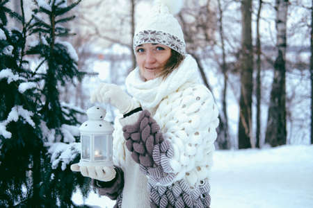 Portrait of a beautiful girl in the winter in the park, in her hands she holds a lantern with candles.の写真素材