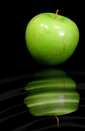 Single green apple isolated on a black background with reflection in a rippling water effect.の写真素材