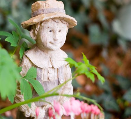 A hand-carved wooden garden boy surrounded by green foliage and pink flowers.の写真素材
