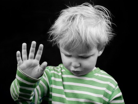 Litlle boy looking down and showing hand on black background, monochrome picture with only color greenの写真素材