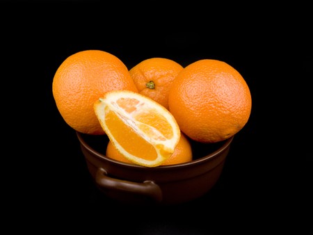 Oranges in ceramic bowl on black backgroundの写真素材