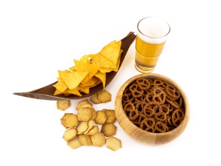 Tortilla chips, glass of beer, bowl of pretzels and some spicy crackers on white background.の写真素材