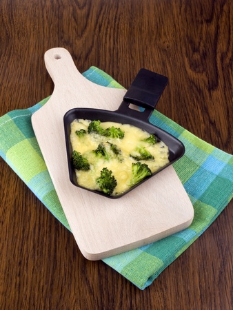Raclette pan with cheese and broccoli on chopping boardの写真素材