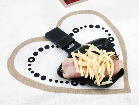 Raclette pan with edam cheese and ham on chopping boardの写真素材