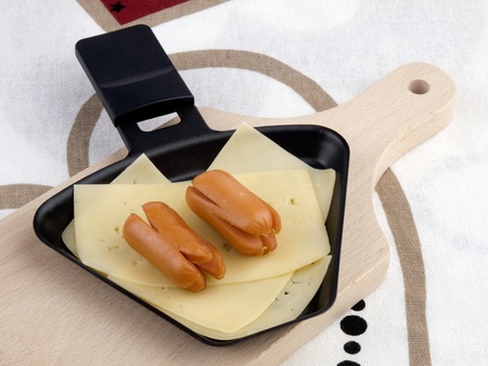 Raclette pan with cheese and cocktail sausages on chopping boardの写真素材