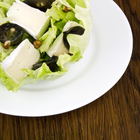 Iceberg lettuce salad with camembert cheese, dark grapes and walnuts on white plateの写真素材