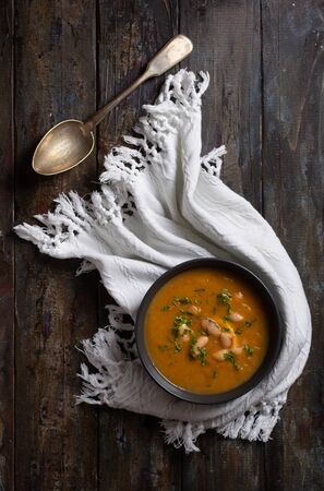 Pumpkin and bean cream soup in dark bowl, spoon, dark rustic wooden surface. Top viewの写真素材