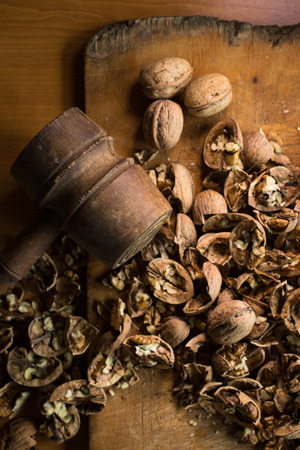 a wooden hammer near a dozen of cracked walnuts