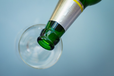 Image of a beer bottle neck over an empty glassの写真素材