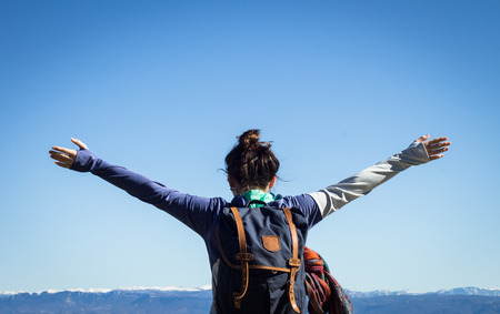 Hiker young woman with arms spread over blue sky and snowy mountain peaksの写真素材