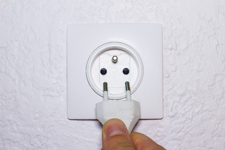 Hand plugs power cord in wall socket