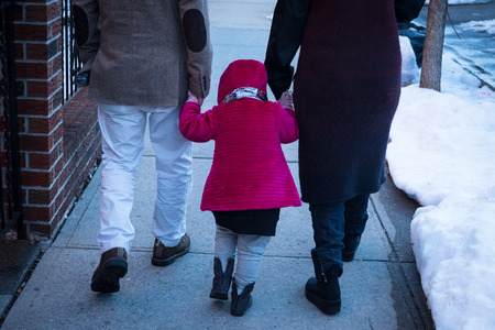 Child holding hands with parents on sidewalk in New York