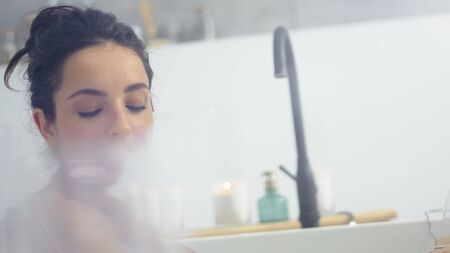 Close up sensual woman lying in bathtub with foam. Romantic girl resting in bathroom at luxury home....