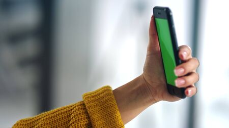 Side view of woman posing for selfie photo indoor. Closeup brunette girl holding smartphone with green screen. Close up girl making video talk on cell phone in slow motionの写真素材