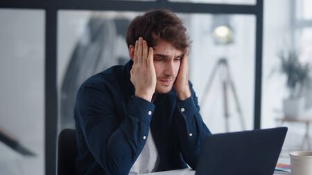 Upset businessman finding mistakes in documents in office. Close up frustrated worker looking at laptop computer at home office. Sad business man reading finance report at notebook indoorsの写真素材
