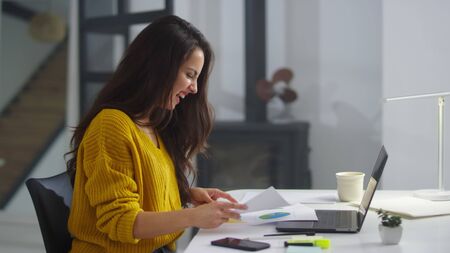 Close up successful woman making winner gestures in slow motion. Happy business woman reading graphs research in documents indoor. Smiling girl looking results in papers in modern officeの写真素材
