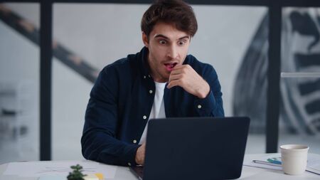 Surprised man getting good news on laptop in office. Happy business man reading positive results at laptop computer. Cheerful winner winning project. Victory man feeling happy.の写真素材