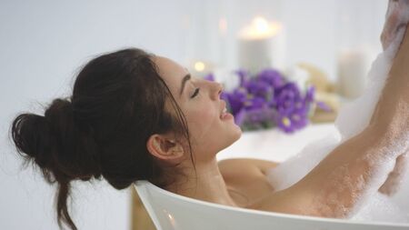 Closeup brunette woman washing hands with foam in slow motion. Elegant girl relaxing in bath with bubbles at luxury hotel. Romantic woman taking bath with candles.の写真素材