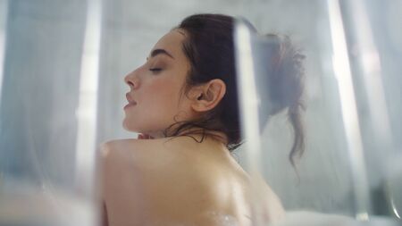 Back view of relaxed woman washing neck in bathtub in slow motion. Closeup hot woman making massage of body at luxury bath. Romantic girl touching skin in foam bath.の写真素材