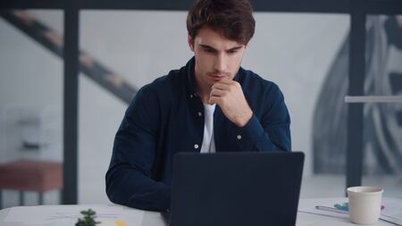 Close up focused business man working laptop in office. Portrait of handsome man reading text on notebook in home office. Serious guy looking laptop computer screen indoor.の写真素材