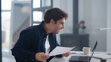 Surprised business man reading financial report indoor. Happy entrepreneur reading results in papers and laptop in slow motion. Close up excited man making yes gestures in office.の写真素材