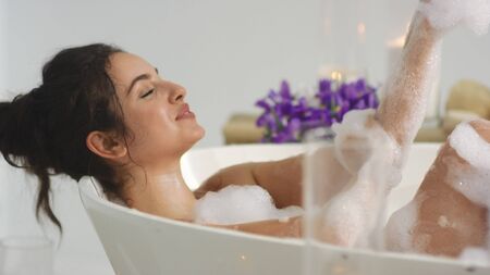 Closeup relaxed woman washing hands in bath in slow motion. Hot girl resting in bath with foam at luxury hotel. Sexy woman touching skin in bath at home.の写真素材
