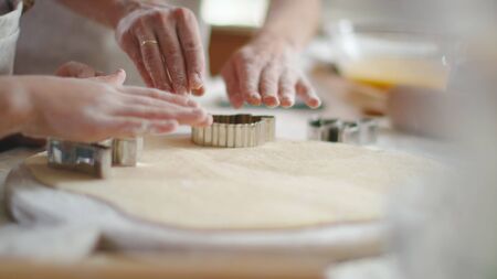 Close up woman and girl hands cutting dough with cookie cutters on kitchen table. Mother helping daughter to make cookies on kitchen in slow motion. Mom and daughter cooking togetherの写真素材
