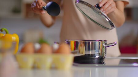 Unrecognizable woman cooking soup on kitchen. Close up of housewife stirring soup with spoon at home in slow motion. Woman chef standing at stove on domestic kitchenの写真素材