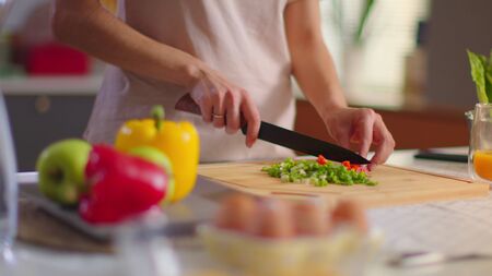 Pretty housewife cutting vegetables on wooden board at kitchen. Woman cooking fresh salad on table. Young lady eating cherry tomato on kitchen in slow motionの写真素材
