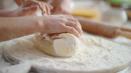 Closeup woman and girl hands kneading dough on kitchen in slow motion. Mother helping daughter preparing dough for cookies on domestic kitchen. Close up child cooking homeの写真素材