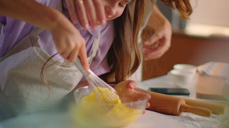 Young mother and daughter whisking eggs in mixing bowl on kitchen in slow motion. Small girl and woman preparing dough for cookies on modern kitchen. Mom and daughter cooking togetherの写真素材