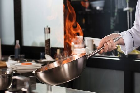 Chef hands hold wok with fire. Closeup chef hands prepare food with fire. Chef man prepare asian food at professional kitchen.の写真素材