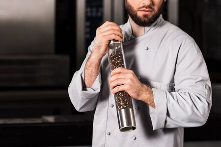 Chef man with pepperbox at kitchen restaurant. Closeup bearded professional with pepperbox. Male chef in uniform with big pepperbox at professional kitchen.の写真素材