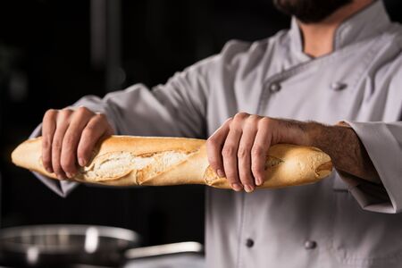 Chef hands with bread at kitchen restaurant. Closeup chef hands with bread. Cooker in uniform keep french bread.の写真素材