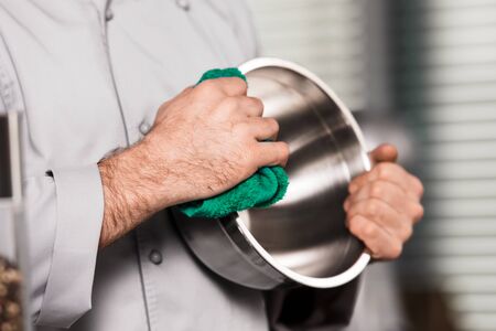 Chef hands wipe bowl with duster. Closeup hands with green duster. Chef male dry steel bowl with green duster at professional kitchen.の写真素材