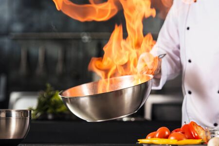 Chef hands hold wok with fire. Closeup chef hands prepare food with fire. Cook burn food at...