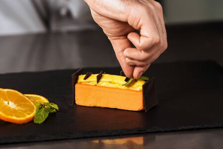 Chef hands decorate orange cake. Closeup hands decorate dessert with chocolate. Professional decorating orange cake with chocolate.の写真素材