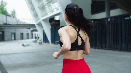 Close up athlete woman running outdoor. Back view of sporty girl jogging on urban street. Closeup female legs running in slow motion. Sport woman running workout at city streetの写真素材