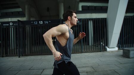 Close up male runner jogging on outdoor workout. Side view of running man on urban street. Fitness...