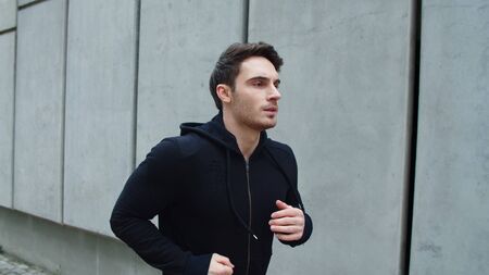Close up sportsman running outdoor in slow motion. Portrait of handsome guy running up stairs on city street. Young runner man jogging on urban street in sweatshirt.の写真素材