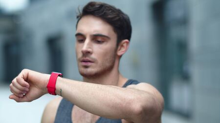 Closeup male athlete using smart clock outside. Portrait of fit man setting smart watch in slow...