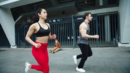 Fitness couple running together on urban street. Athlete man and woman jogging at morning training. Sport couple training run exercise outdoor in slow motion. Man training obstacles run.の写真素材
