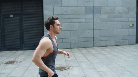 Sporty man running outdoor. Male runner jogging on city street in slow motion. Fit guy training run...